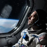 Astronaut gazes from space station window with exhausted relief and blue starlight illuminating their face