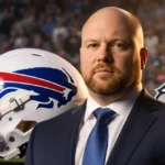 Brian Daboll stands confidently in suit with football helmet and Buffalo Bills colors showing in background