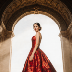 Bride standing under ornate wedding arch in bright red dress with golden sunlight casting glow on her surprised face