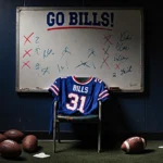 Worn stadium seat holds abandoned Bills jersey with faded Go Bills sign and blanked-out plays on whiteboard behind