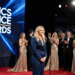 Chelsea Handler standing at microphone with Critics Choice Awards logo screen and glamorous red carpet attendees
