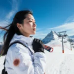 Chloe Kim stands on snowy slope with skis over shoulder and mountain peaks behind her showing determination
