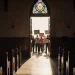Protesters gather outside church with signs visible through stained glass windows and empty pews inside