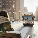 Young commuter sits on snow-covered bench wrapping scarf with warm sun glowing over snow and a SEPTA bus passing by.