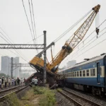 Construction crane collapsing onto moving train with debris and emergency response visible