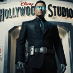 Doorman standing confidently with metallic high‑tech suit and Hollywood Studios logo on modern building.
