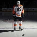 Christian Dvorak standing on Flyers ice rink with introspective gaze and a lone puck under muted lighting