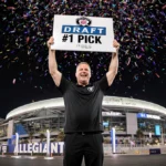 Raiders coach holding giant 2026 NFL Draft #1 Pick sign with stadium lights on and confetti-filled sky over Las Vegas.