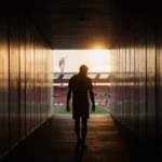 Riqui Puig walking toward a dim tunnel with golden light at the end and a blurred stadium silhouette in the background