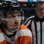 Philadelphia Flyers defenseman Abols looks up with concern while receiving assistance on the ice with arena lights glowing be