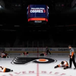 A medical trainer tends to an injured Flyers player on the ice with the Philadelphia Flyers logo visible and the scoreboard s