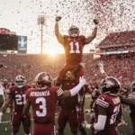 Indiana University team leaping and hoisting each other with Coach Curt Cignetti QB Fernando Mendoza raising arms sunset ligh