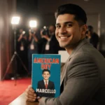 Marcello Hernández smiles holding American Boy with natural light and a red carpet backdrop signaling Netflix special