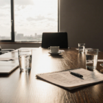 Pen lying between two glasses on a wooden minimalist office boardroom table with a strategy map scribble