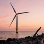 Offshore wind turbine spinning with sunrise over Atlantic waters and rugged coastline in foreground