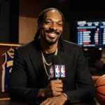Snoop Dogg sits confidently with microphone and NBA jerseys behind him showing his new analyst role