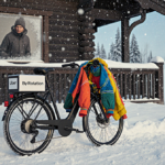 Uber Courier bike parked with colorful outfits on handlebars and a By Rotation package on seat near a snow ski resort lodge