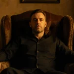 Stephen Graham sits in worn armchair with vintage TVs and VHS tapes showing nostalgic glow