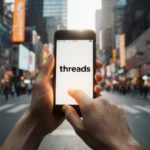 Person scrolling social media on phone with Threads logo and city street with shops in background