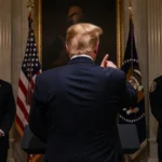 Donald Trump gesturing at podium with American flag behind him and police officers standing guard
