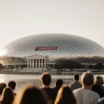 Excited Washington Commanders fans walk toward the new silver domed stadium with Lincoln Memorial and Tidal Basin reflecting