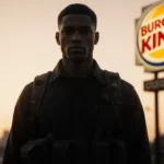 Young man standing before dim Burger King sign with dusk glow and tactical gear