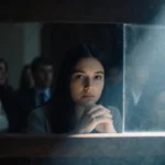 Young woman sits in courtroom with hands clasped showing determination while jury watches