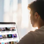YouTuber relaxing at desk with blurred screen showing channels and pastel background